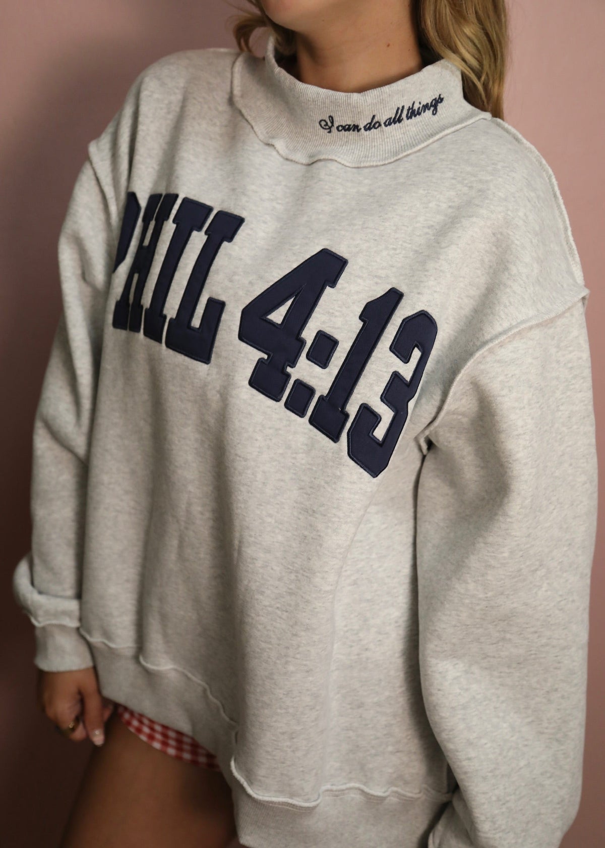 Gray sweatshirt with 'PHIL 4:13' text worn by a person against a plain background