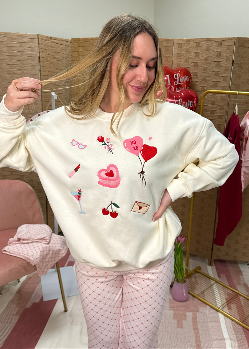 Woman wearing a white sweatshirt with colorful designs in a room with a pink chair and clothes rack.