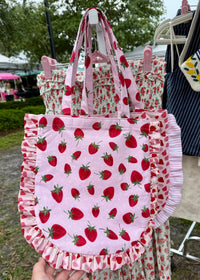 Pink tote bag with strawberry pattern held by a hand outdoors