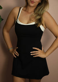 Woman wearing a black dress with white trim against a beige background