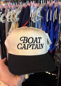 Cap with 'BOAT CAPTAIN' text held in front of a clothing rack.
