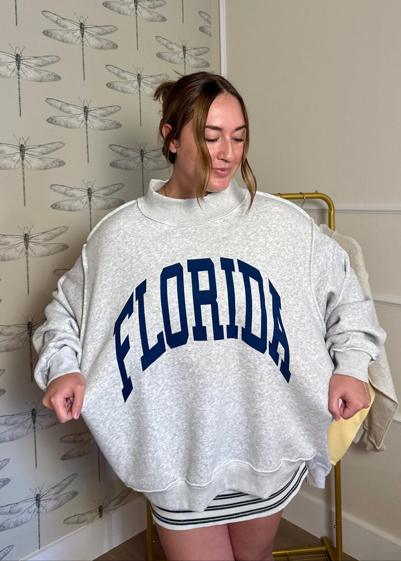 Person wearing a gray sweatshirt with 'FLORIDA' printed on it, standing in a room with dragonfly-patterned wallpaper.