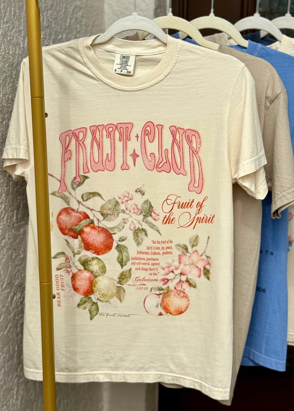 T-shirts with 'Fruit of the Spirit' design on a rack against a neutral background