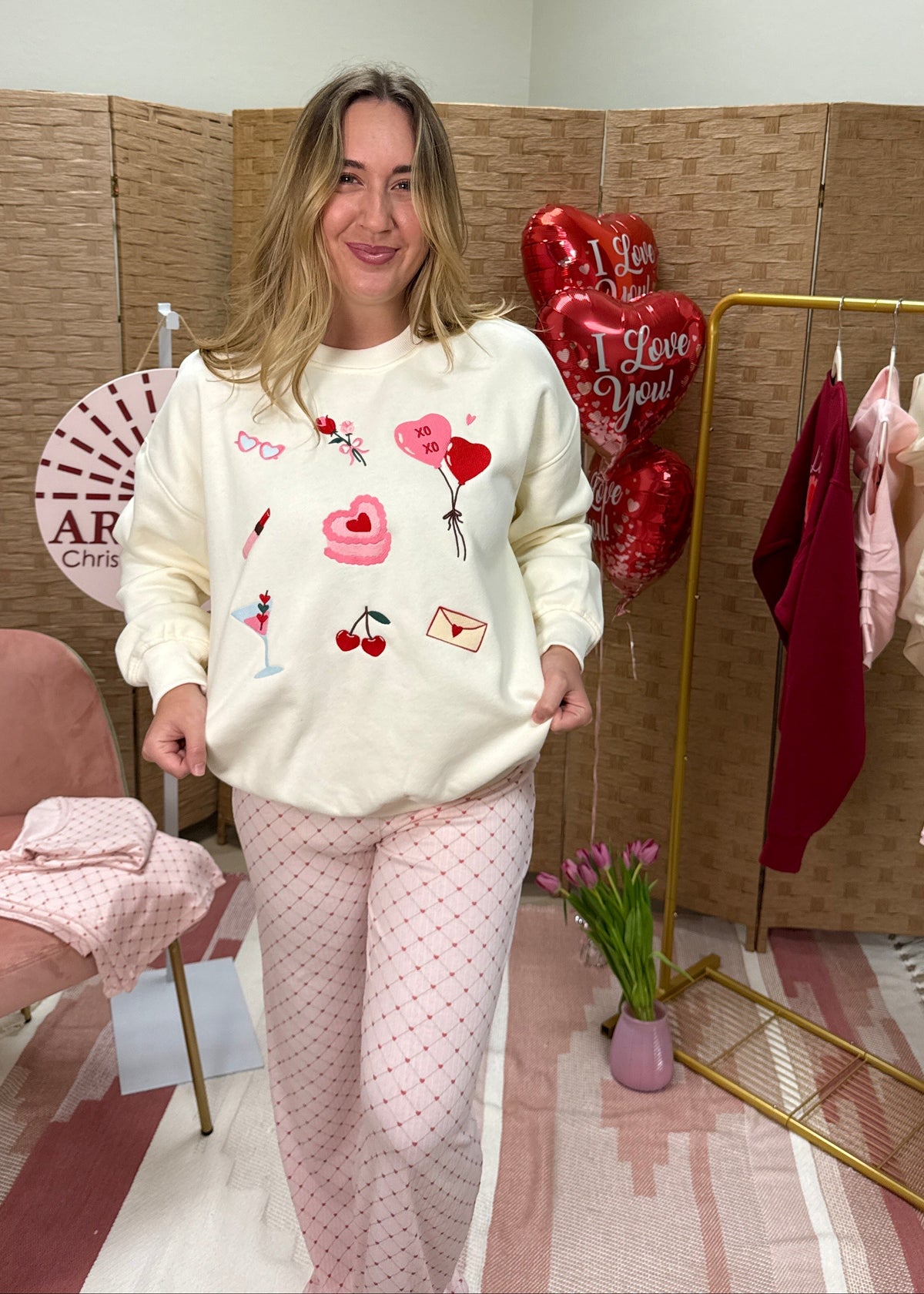 Woman in a room with a pink chair, clothes rack, and heart-shaped balloons.