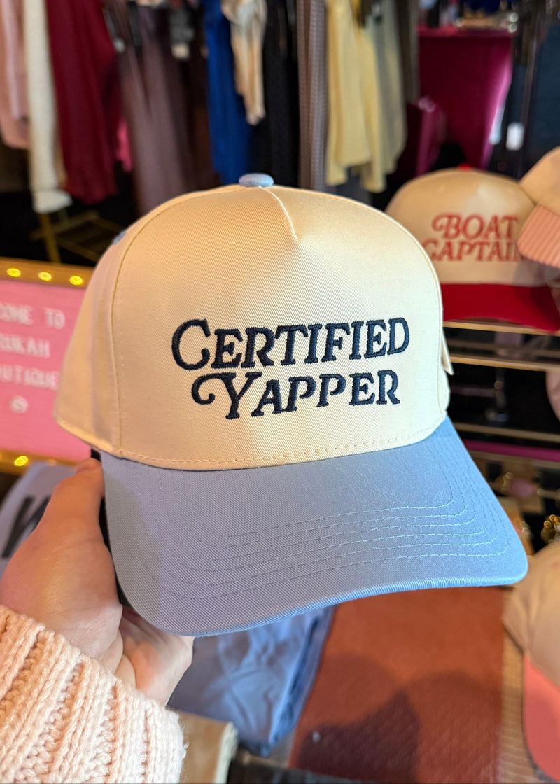 Beige and blue cap with 'CERTIFIED YAPPER' text in a clothing store setting