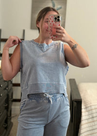 Person wearing a light blue sleeveless top and pants in a room.