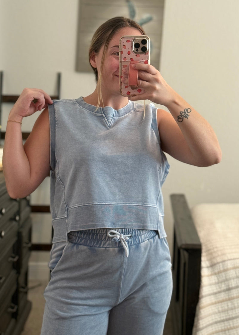 Person wearing a light blue sleeveless top and pants in a room.