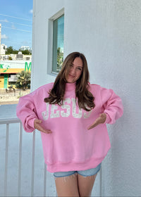 Person wearing a pink sweatshirt with 'JESUS' printed on it, standing on a balcony.