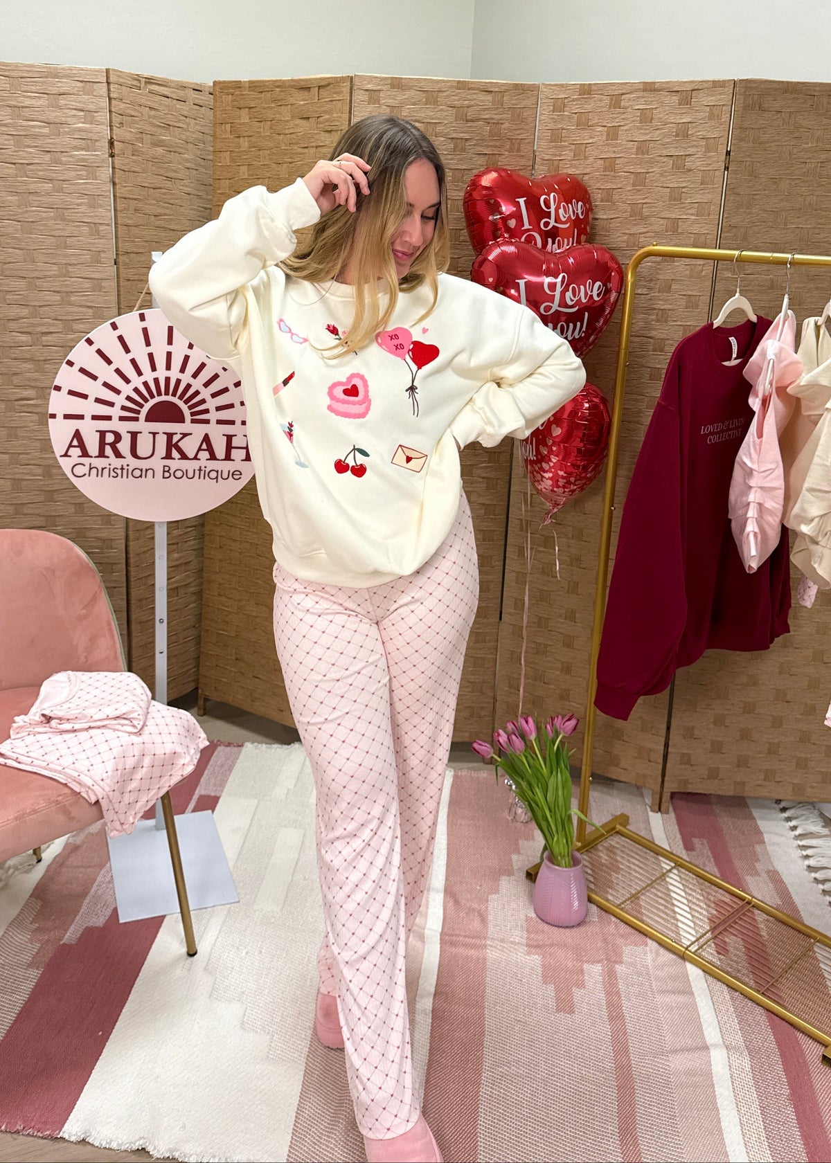 Woman in a store wearing a white sweatshirt with floral designs and pink pants, standing next to a clothing rack.