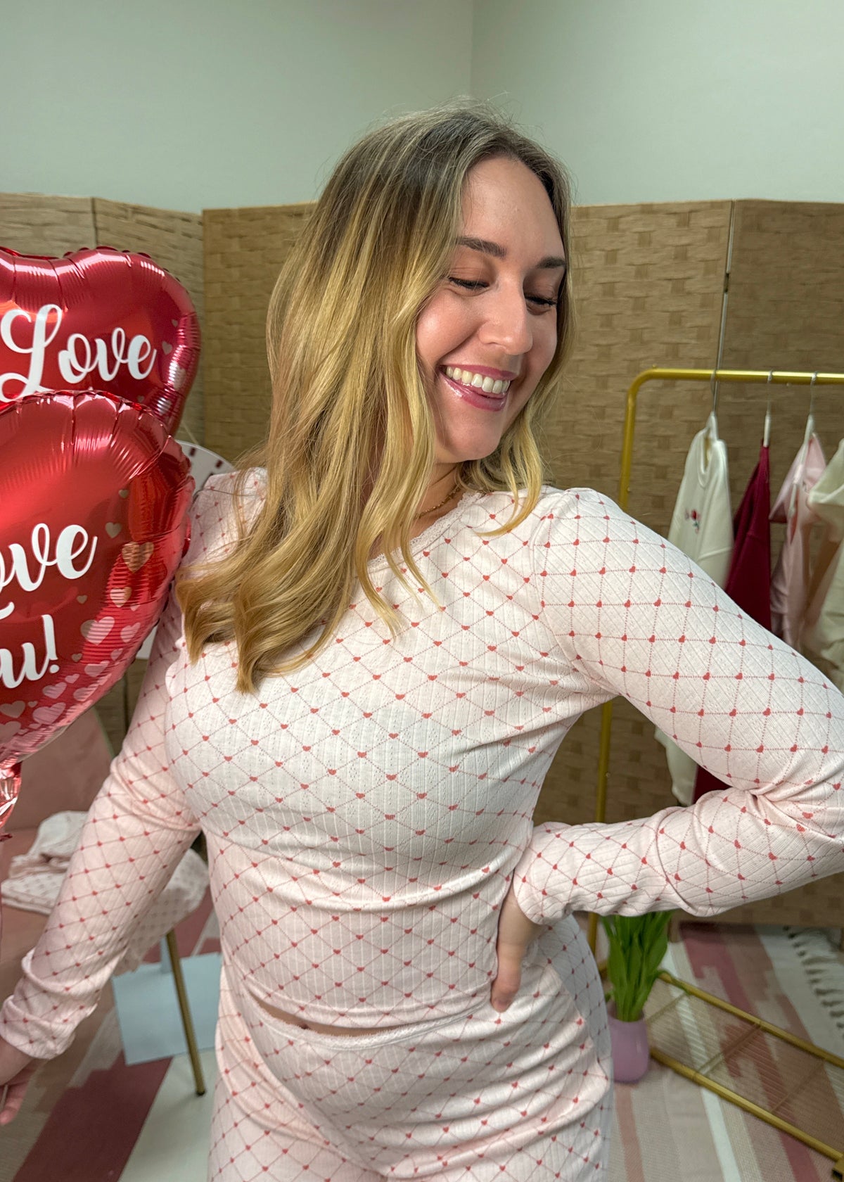 Woman holding heart-shaped balloons with 'Love' and 'You!' text showcasing heart pattern pajamas