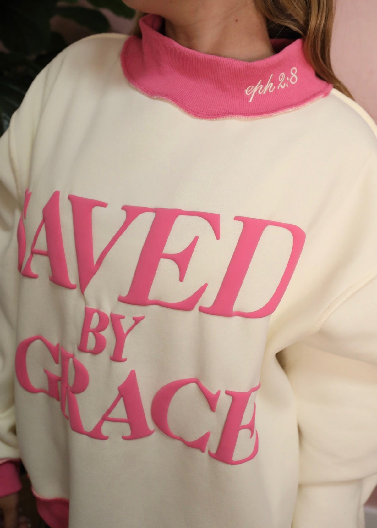 White sweatshirt with pink text 'Saved by Grace' worn by a person.