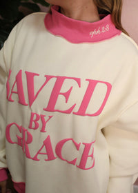 White sweatshirt with pink text 'Saved by Grace' worn by a person.